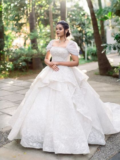 A stunning portrait of a bride in a magnificent white wedding gown. She stands on a gravel path, surrounded by the lush greenery of our venue, looking like a princess in a forest.