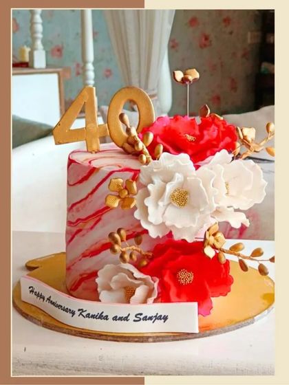A stunning 40th-anniversary cake with a red marble effect, adorned with beautiful white and red sugar flowers and gold accents.