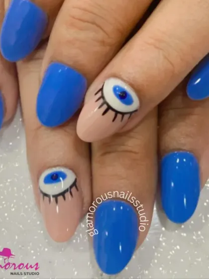 Ward off bad vibes with these stylish evil eye nails. The design combines a solid bright blue with nude accent nails featuring a hand-painted evil eye and eyelashes.