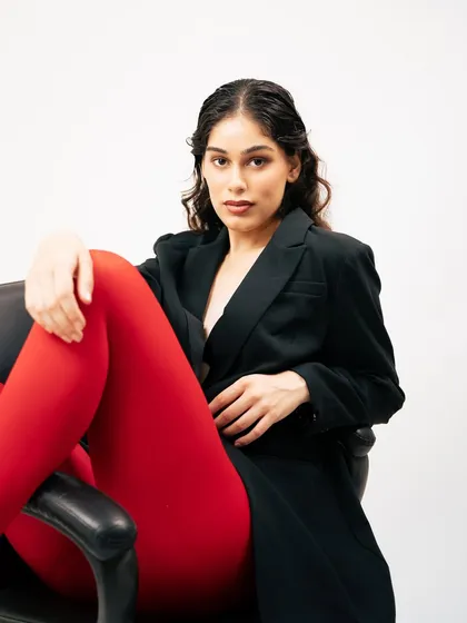 A bold and graphic studio portrait for a high-fashion editorial. The striking contrast between the black blazer, white background, and vibrant red tights creates a powerful, modern image that immediately grabs attention.