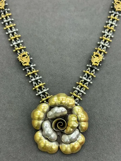 This dual-tone necklace showcases a modern floral design. The pendant features layered gold and silver petals with a spiral centre, attached to a unique chain of alternating silver and gold-plated links.