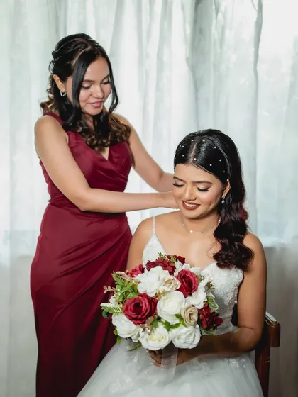 A sweet moment between the bride and her bridesmaid. Her hair is styled with delicate pearl accessories, and her makeup is soft and romantic.