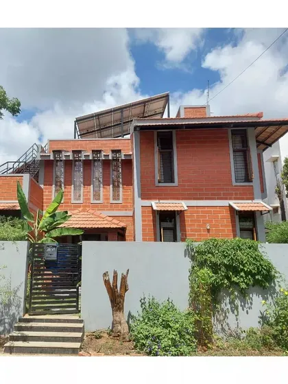 The exterior of this home in Secunderabad showcases exposed brick, prominent jaali windows, and rooftop solar panels, demonstrating a commitment to both aesthetics and energy efficiency.
