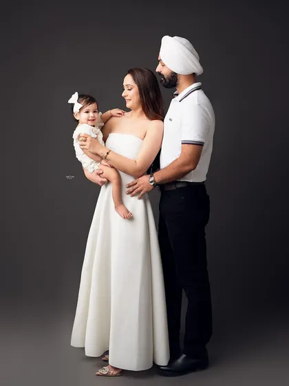 An elegant family portrait against a classic grey backdrop. The coordinated white outfits create a timeless look.