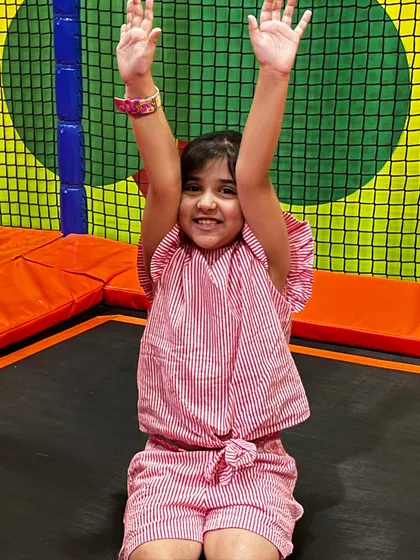 Hands up for fun! A girl celebrates on the trampoline, enjoying the freedom to jump and play.