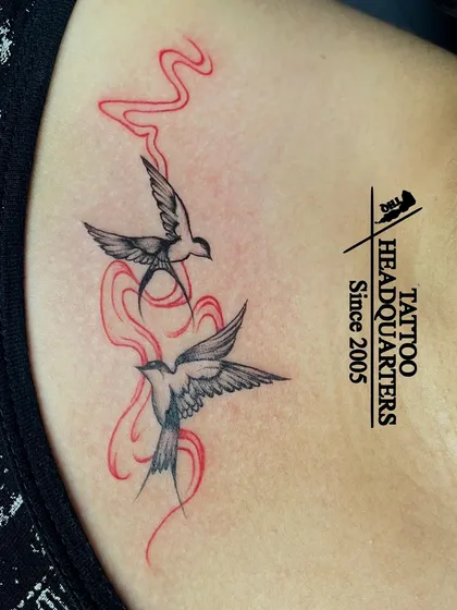 A tattoo of two swallows in flight, with red smoke-like trails, creating a dynamic and artistic piece.