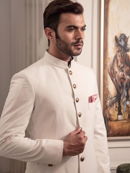 A pristine white sherwani, the epitome of classic elegance. The gold buttons and pink pocket square provide a subtle pop of color, making it a perfect choice for a sophisticated groom.
