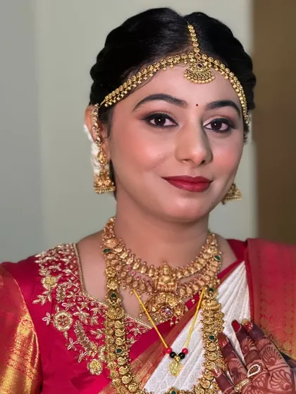 A classic bridal close-up that highlights the key elements of a muhurtham look. Notice the flawless skin, the beautifully shaped matha patti, the traditional gold jewelry, and the rich red lip that brings it all together.
