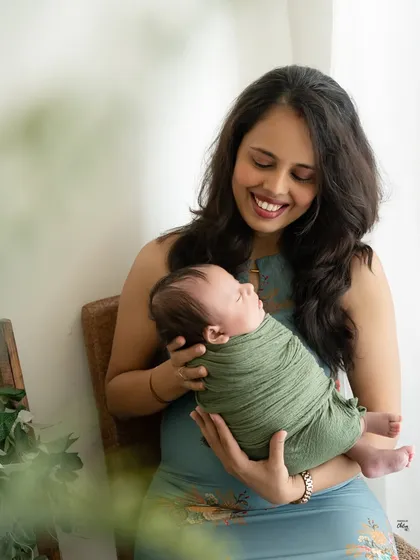A mother's joyful smile as she holds her sleeping baby. The natural light and earthy green tones of the swaddle give this portrait a fresh and organic feel.