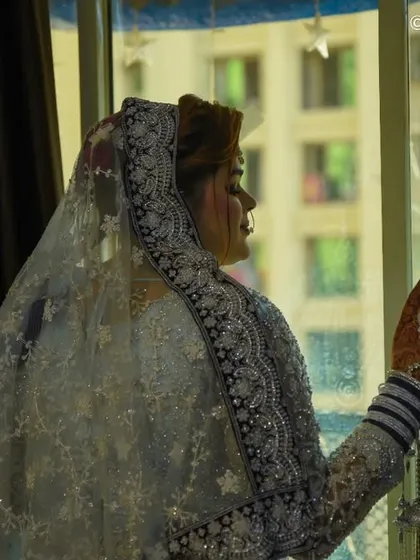 A moment of quiet reflection by the window. The natural light creates a soft, dramatic silhouette, highlighting the bride's profile and the elegant embroidery on her veil.