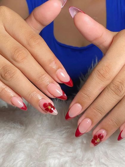 A sharp stiletto set with a deep red French tip and accent nails featuring beautiful, hand-painted red flowers.