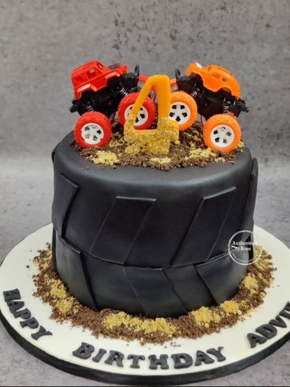 A monster truck cake for a 4th birthday. This cake is designed to look like a giant tire, with two monster trucks on top of edible dirt.