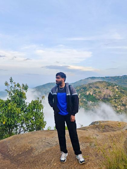 Taking a moment to soak in the incredible view from the top. A trekker stands on a rock ledge, looking out over the fog-covered hills.