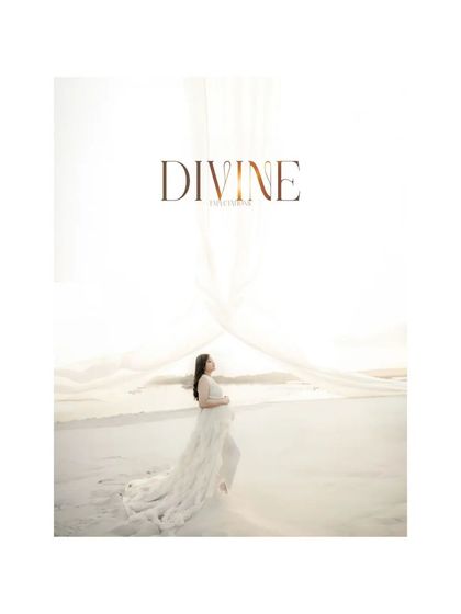 "DIVINE." An artistic and minimalist shot of the mother-to-be on a sandy shore, with a flowing white gown and sheer fabric creating an ethereal and divine look.