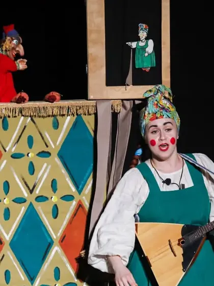 A performer plays a traditional instrument while watching the 'Petrushka' puppet show, adding live, authentic music to the experience.