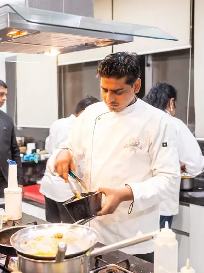 A chef carefully transfers a freshly cooked item from a pan, focused on the task at hand. This level of concentration is key to our quality.