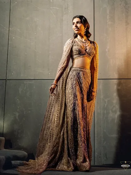 A full-length portrait of the bride, her sparkling gown and confident pose captured against a modern, textured wall.