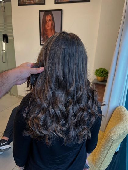 My hand holding up a section of this cool-toned balayage to show the detail in the color work and the healthy shine of the hair.