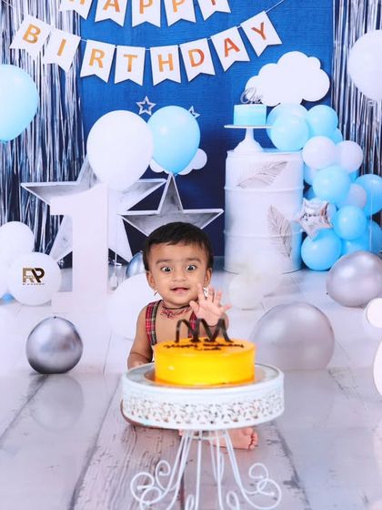 A candid moment of discovery as the birthday boy explores his first birthday cake. The blue and silver hot air balloon theme adds a touch of adventure to the celebration.