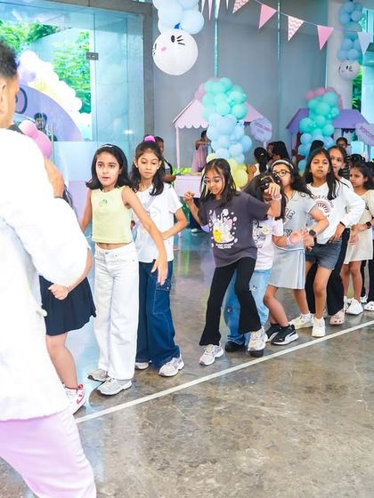 A party host leading a line of young girls in a fun, interactive dance game at a Hello Kitty themed event.