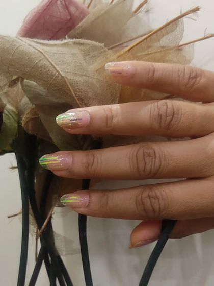A single hand showing the sheer nail extensions with green iridescent flakes, a very subtle and unique style.