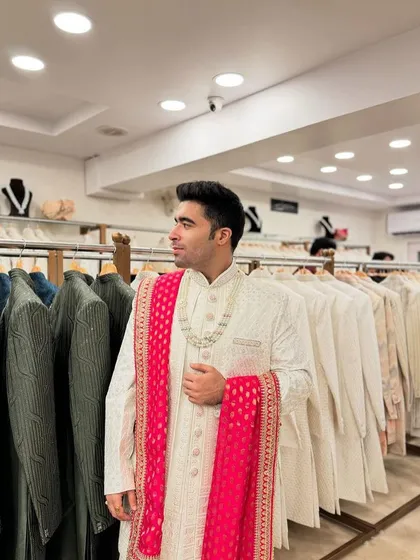 A customer trying on a classic ivory sherwani with a vibrant pink bandhani stole, adding a pop of color to a timeless groom's outfit.