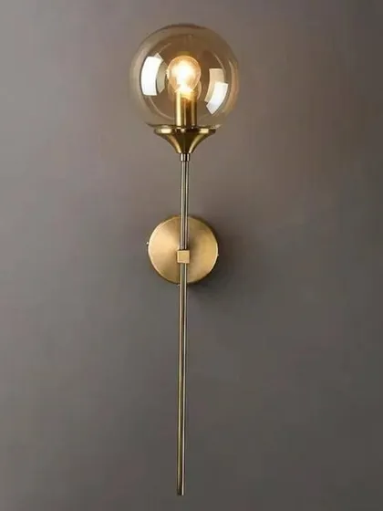 This industrial-inspired globe sconce features a tinted glass ball on a slender gold-finished metal rod. The transparent shade allows the bulb to be a design element, adding a vintage touch to a modern fixture.