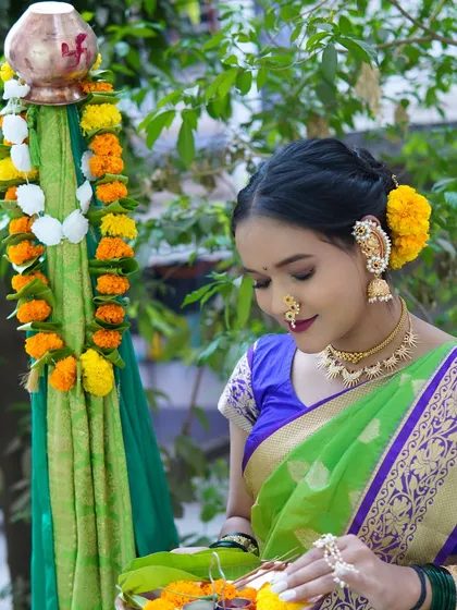 A serene moment by the Gudi. The makeup is soft and natural, with hair tied back in a bun adorned with yellow flowers, reflecting the festive colors.