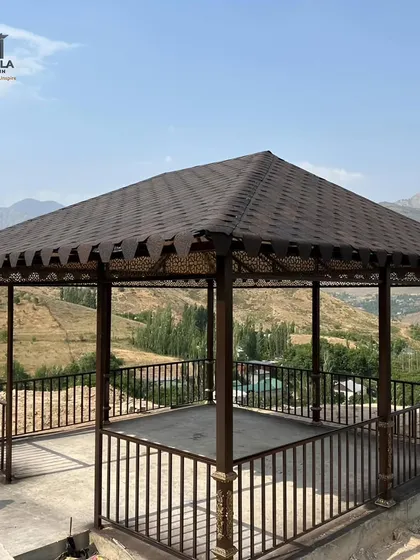 A classic gazebo structure with a durable shingle roof and decorative metal railings, set against a scenic mountain backdrop. This design is perfect for creating a focal point and sheltered seating area in a park or large garden.