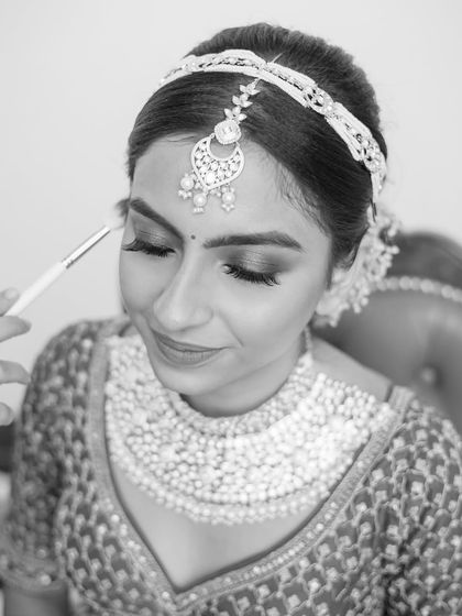 A black and white shot of a bride getting her makeup done, a moment of calm before the ceremony.