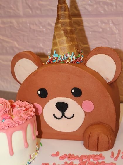 A beary special half birthday cake. This design features a large, friendly bear-shaped cake wearing an ice cream cone party hat.