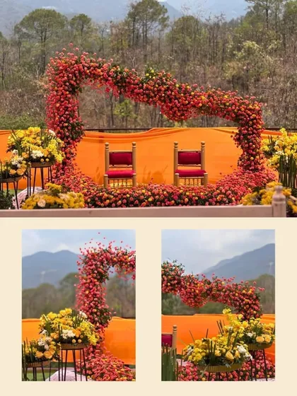 A closer look at the unique heart-shaped floral arch for a haldi ceremony. The bright red and orange flowers create a beautiful frame for the couple's chairs against the mountain backdrop.