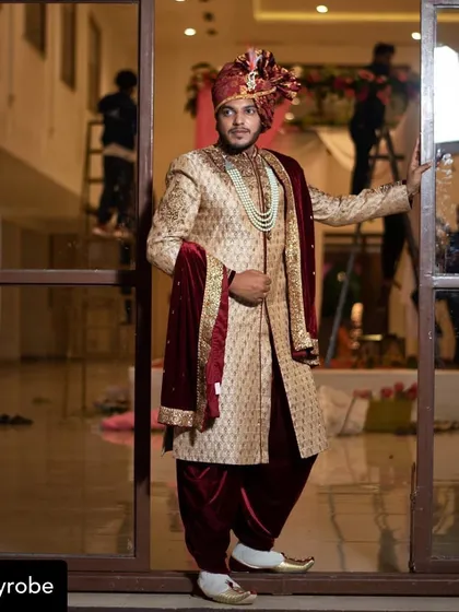 A real client looking regal and ready for his baraat. He is wearing a beige and maroon sherwani set, complete with a safa, mala, and dhoti-style pants.