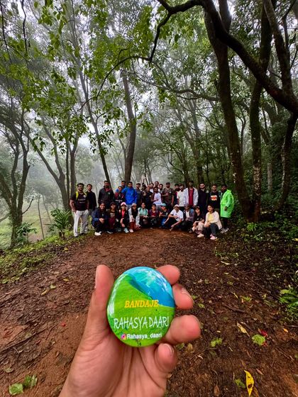 The Bandaje trek badge held against the backdrop of the misty forest trail.