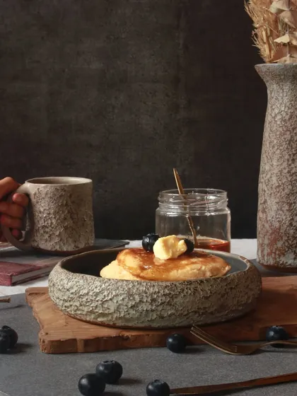 A breakfast scene featuring pieces from 'The Rock' Collection. The textured mug and bowl are perfect for everyday rituals, adding a touch of bold, unpolished beauty.