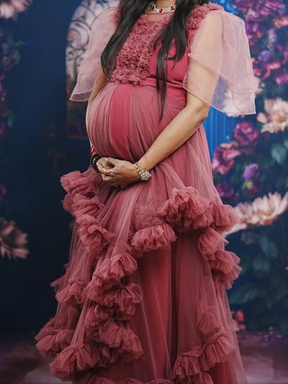 This pastel onion pink gown with delicate flutter sleeves is a soft and flowy option for a maternity photoshoot. It's available to rent with matching jewelry.
