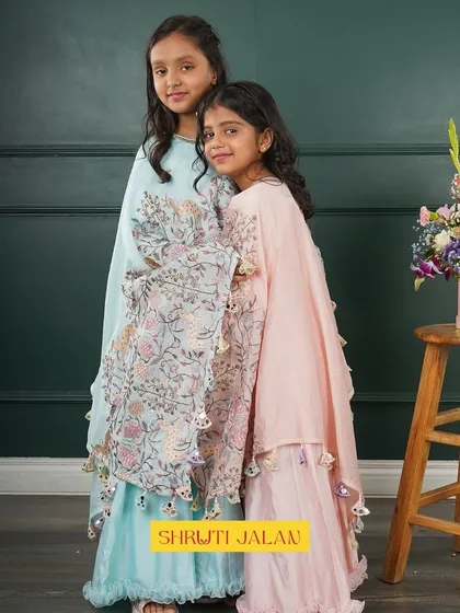 Sisters in pastel cape gowns, sharing a sweet moment. The soft blue and pink complement each other beautifully.
