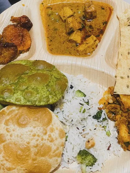 A look at our complete homestyle thali. This one features fluffy pooris, including a vibrant palak poori, served with paneer curry, vegetable rice, a dry vegetable side, papad, and fried potatoes.