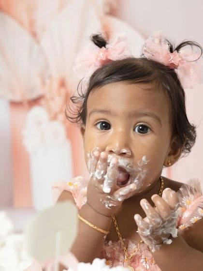 A sweet one-year-old girl enjoying her pink-themed cake smash session. I love capturing these close-ups of their frosting-covered fingers and happy faces.