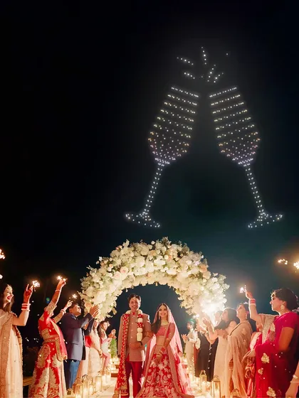 Let's toast to your new beginning in the grandest way possible. Here, I've created giant, clinking champagne glasses in the sky, perfectly timed to celebrate the couple's union as their guests cheer them on with sparklers.