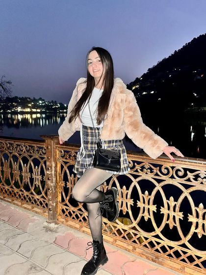 Posing by the lake in Nainital. This winter look with a plaid skirt, boots, and a faux fur jacket is both stylish and practical for a cold destination.