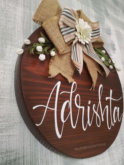 A side angle of the "Adrishta" name plaque, showing its thickness and the rich texture of the wood grain and burlap bow.