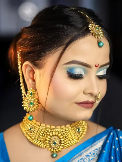 A vibrant blue and white cut-crease eye makeup look, paired with heavy gold jewelry. This is a bold, festive look that demonstrates precision and creativity.