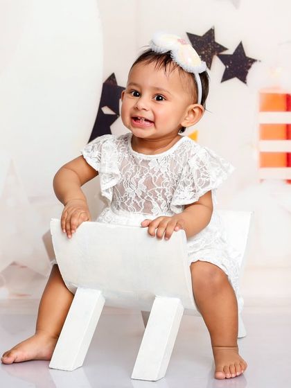 A big, happy smile from our little star. The simple white dress and background make her joyful expression the focus of the photo.