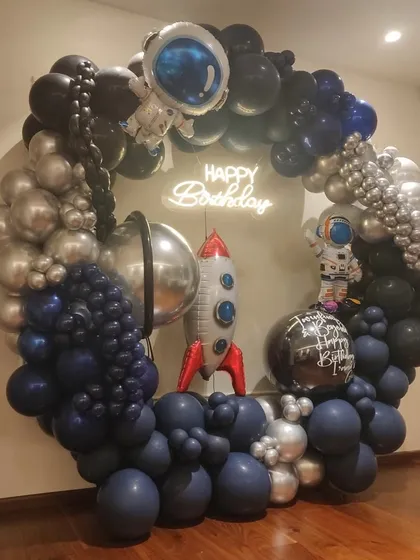 To infinity and beyond! We created this spectacular spaceship-themed organic balloon ring for a young astronaut's birthday. The design features a full circle of balloons in deep space blues, blacks, and metallic silvers, complete with astronaut and rocket ship foils, and a glowing "Happy Birthday" neon sign at the center.