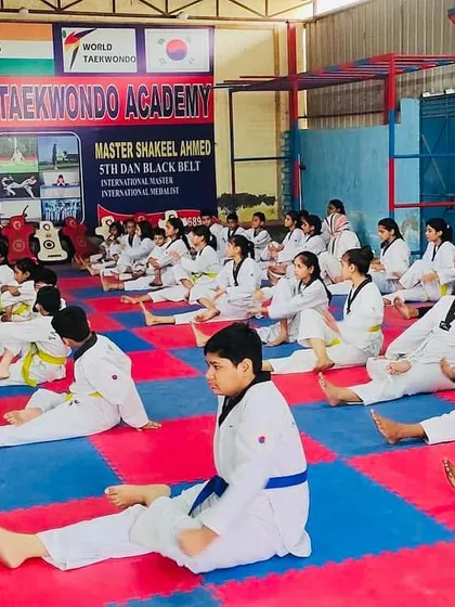 Discipline starts with the basics. A class of students in doboks of various belt colors performs synchronized stretching exercises on the safety mats of our dojang.