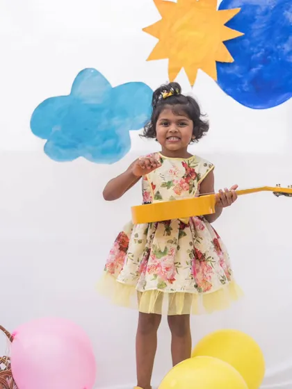 A sweet girl playing her ukulele in a yellow floral dress. The comfortable design and happy print make it a perfect outfit for creative play.