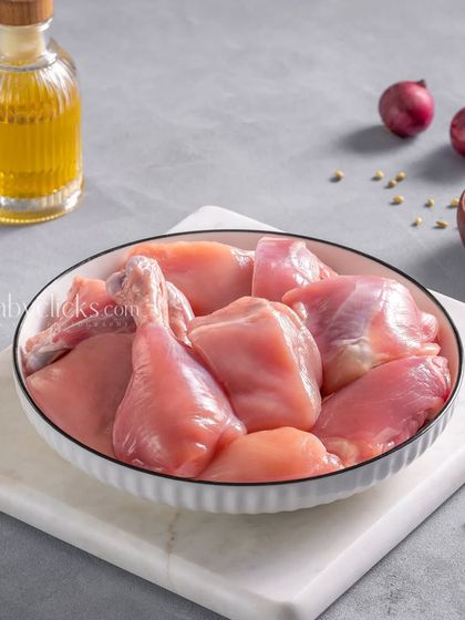 Raw, curry-cut chicken pieces in a white bowl on a marble slab, a simple and clean product shot.