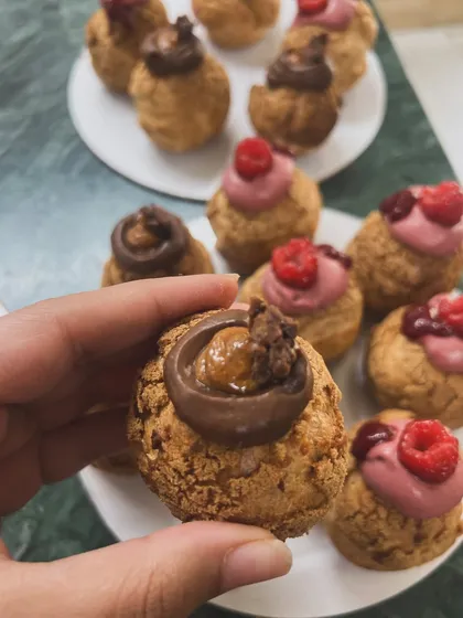 A hand holding up one of my chocolate caramel choux pastries, showing the texture and filling. It's a little bite of handcrafted love.
