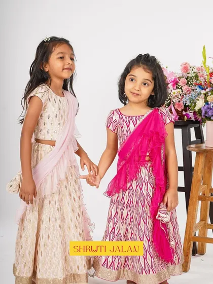 Two sisters hold hands, dressed in my printed lehengas. The different colorways in pink and cream show how sisters can coordinate their looks.